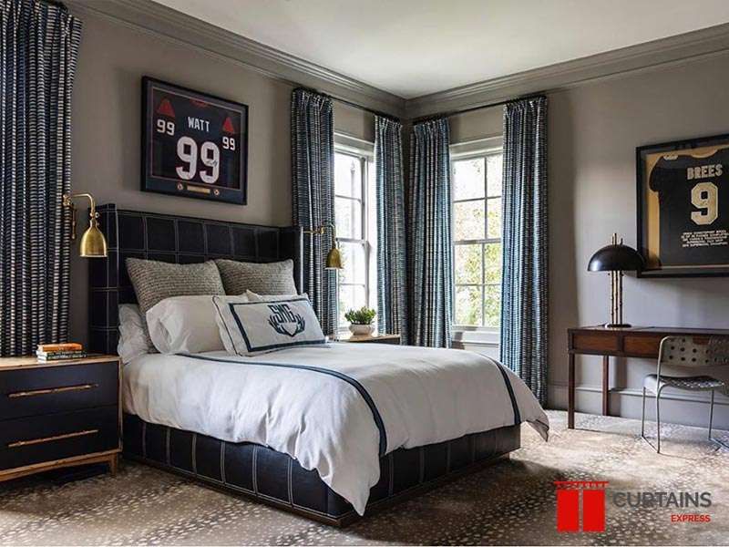 Blue and white patterned curtains at two windows flanking a dark leather bed, brass swing-arm lamps either side
