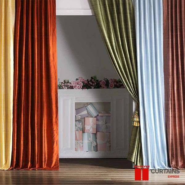 Silk curtain panels in gold, rust, olive, pale blue and copper hung side by side as a colour display