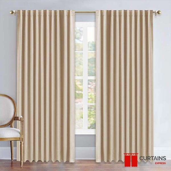 Cream back-tab curtains on a gold pole either side of a white casement window, carved armchair to one side