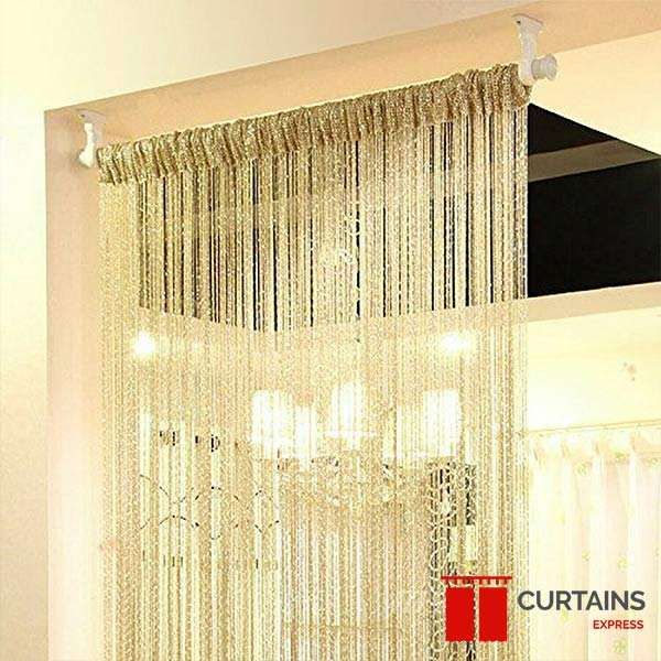 Gold string curtain on a white rod filling a doorway opening, chandelier light glowing through the strands