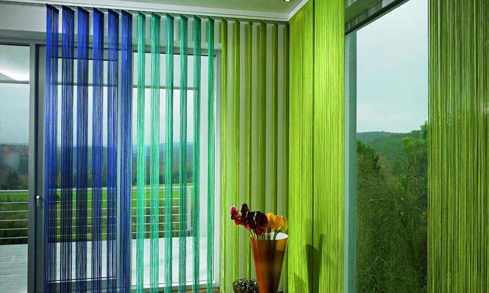 Blue, teal and lime string curtains hung across glass doors opening onto green hills and trees