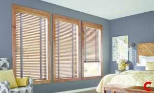 Honey oak venetian blinds on three windows in a slate-blue bedroom with a matching wooden headboard