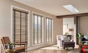 Taupe wooden venetian blinds on a run of tall living room windows lit from a skylight overhead