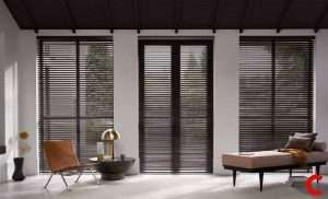 Dark brown venetian blinds across three floor-to-ceiling glass doors, with a leather chair and daybed inside