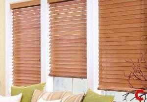 Honey wooden blinds lowered over three bay windows above a sofa cushioned in green and cream