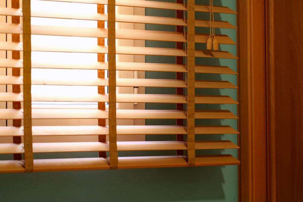 Close-up of pale pine blind slats tilted open at a window, set against a green wall and stained wood door frame