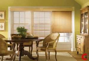 White wooden blinds on a wide window next to honey oak blinds on the adjoining one, above a round dining table