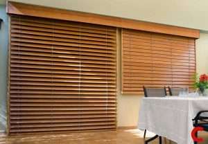 Mid-brown wooden blinds covering a wide sliding door and a second window under a timber pelmet, beside a laid dining table