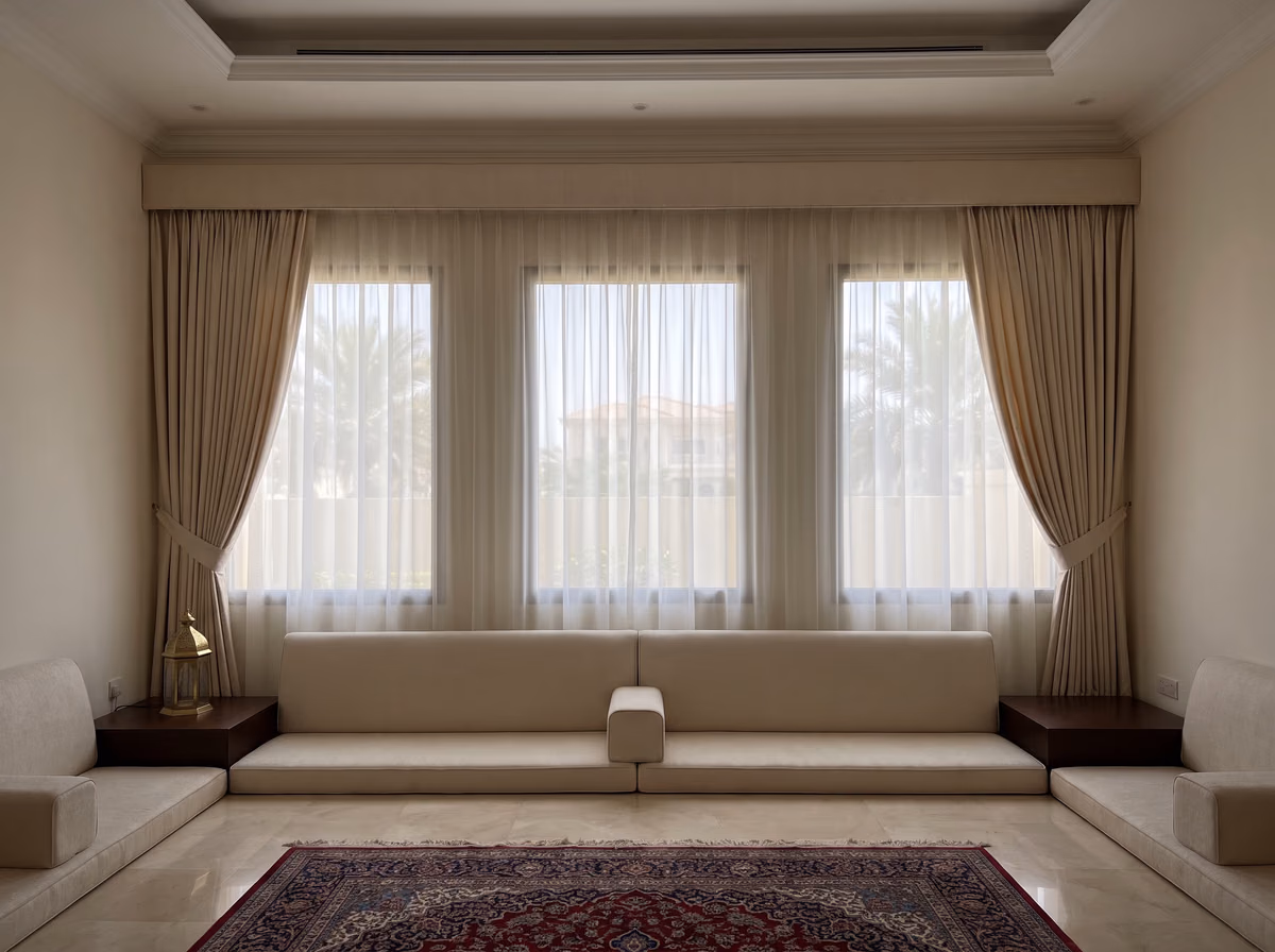 Villa majlis with champagne curtains held back under one fabric-covered pelmet, a white sheer across three windows and low seating