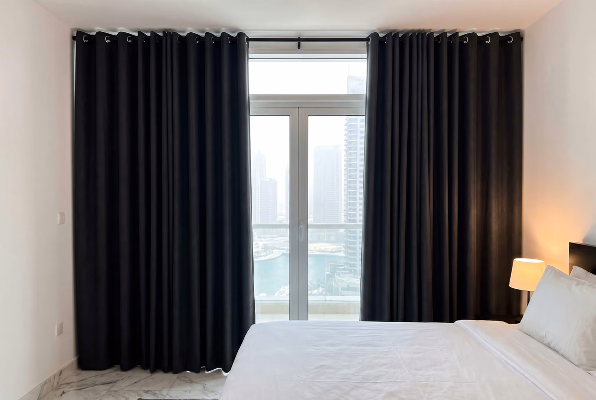 Bedroom with charcoal blackout eyelet curtains on a black pole under the ceiling, open onto a balcony above Dubai Marina