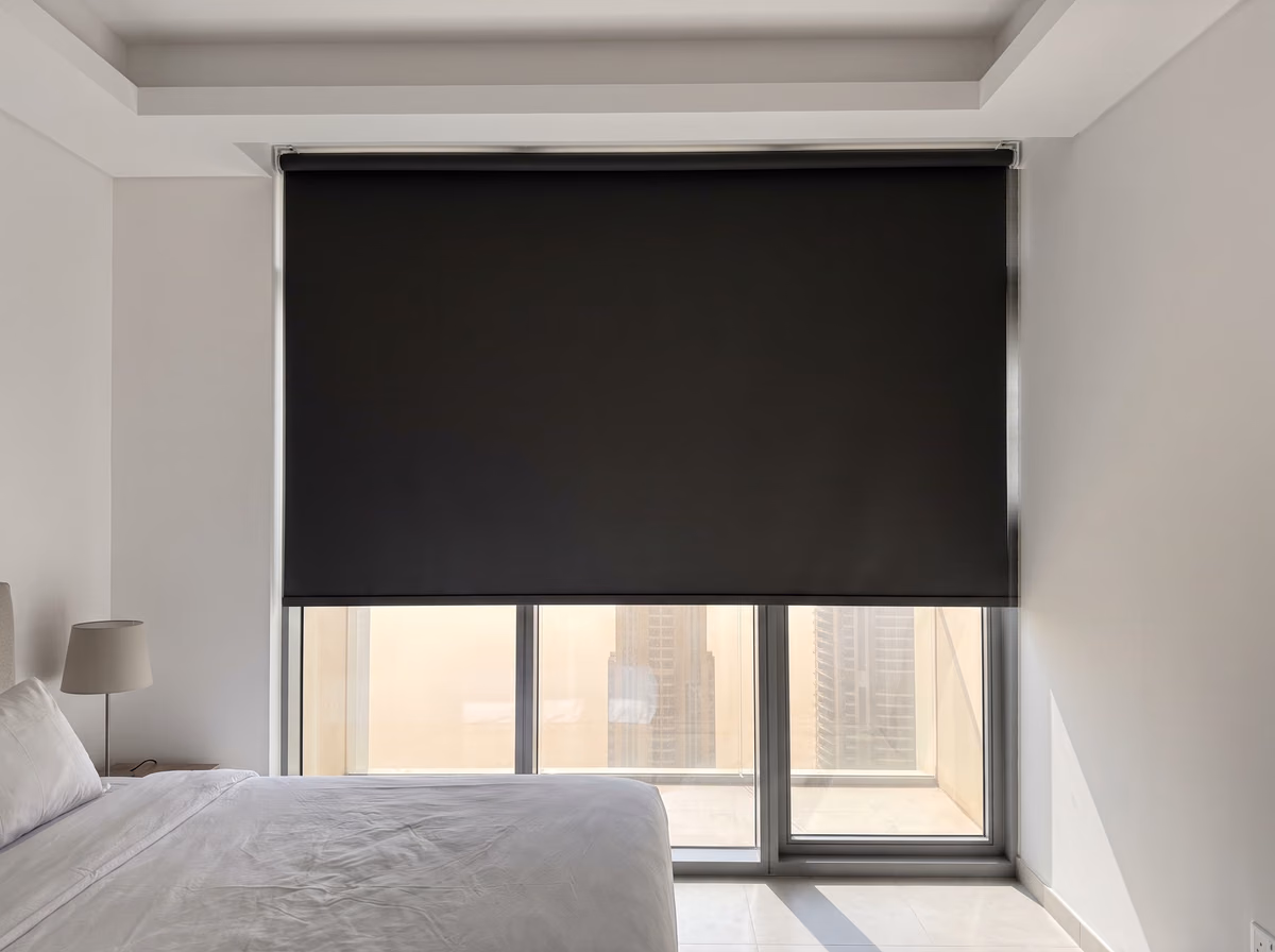 Charcoal blackout roller blind fixed up inside a ceiling curtain pocket, lowered most of the way over tower bedroom glass