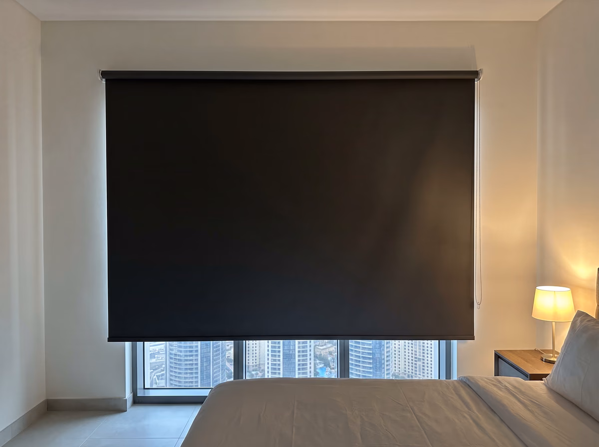 Tower bedroom with a charcoal blackout roller blind fixed on the wall over the window and lowered most of the way, a bedside lamp lit