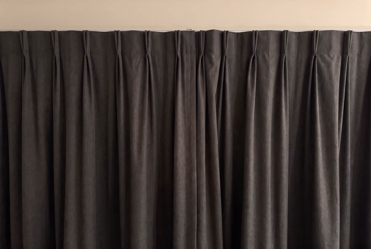 Charcoal pinch-pleat curtains hung close under a white ceiling