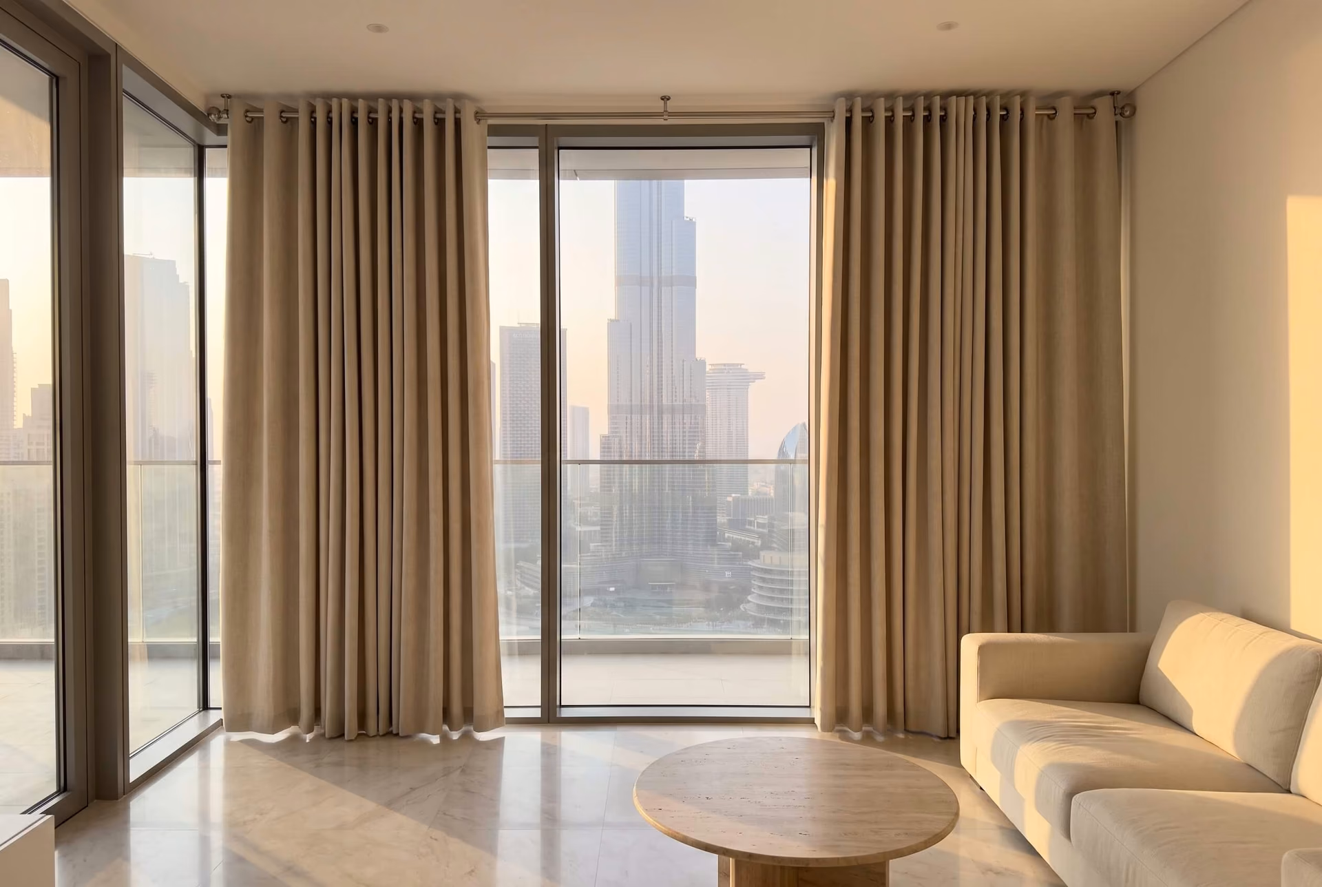 Living room with oatmeal eyelet curtains on a ceiling-fixed steel pole, open beside balcony glass facing the Burj Khalifa