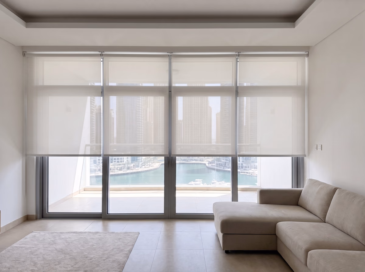 Four white sunscreen roller blinds lowered to one height across balcony glass in a tower living room, a marina and towers beyond