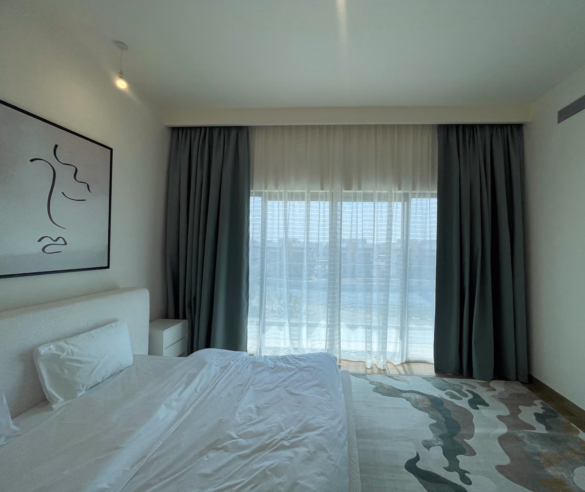 Grey blackout curtains stacked either side of a bedroom's glass door, a white sheer drawn across it and a white bed in front