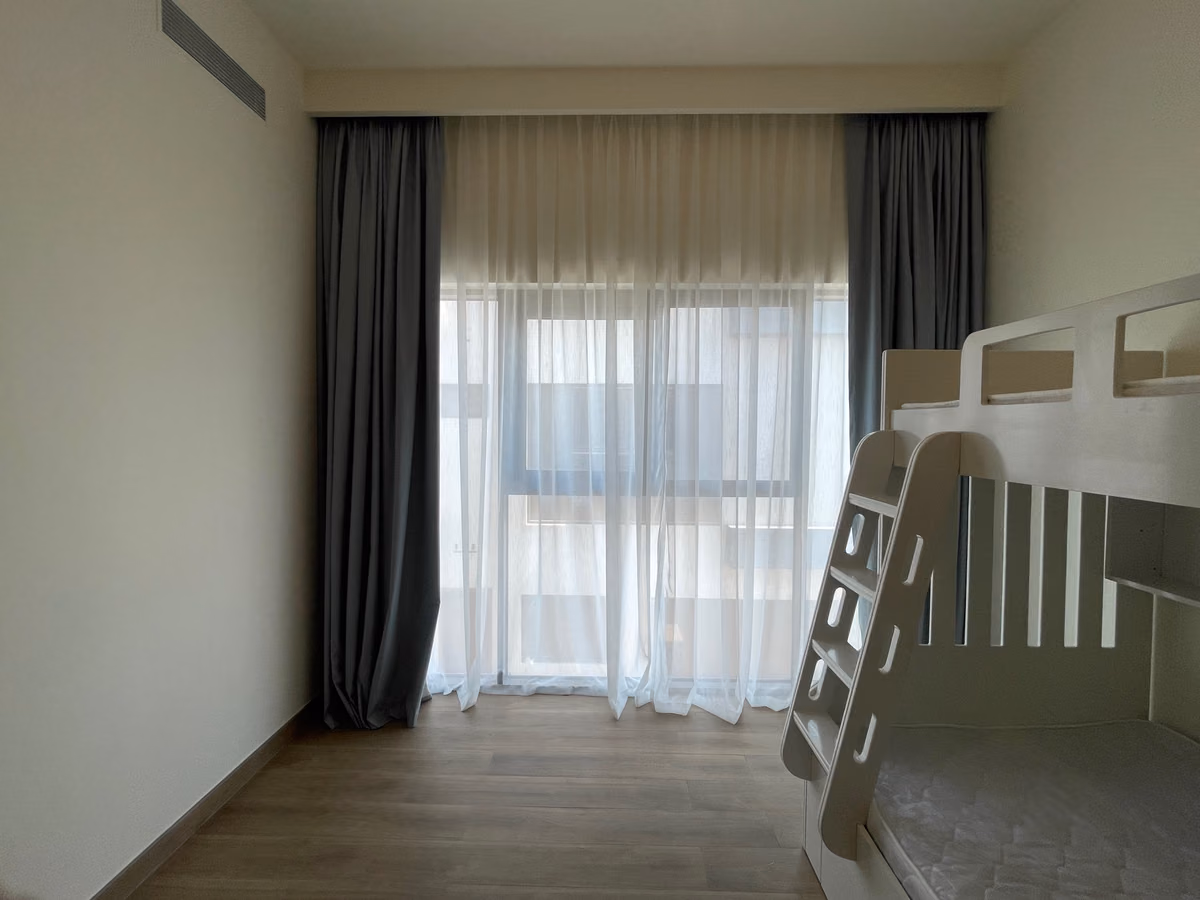 Grey blackout curtains stacked either side of a kids' bedroom window, a white sheer drawn across and a white bunk bed to the right