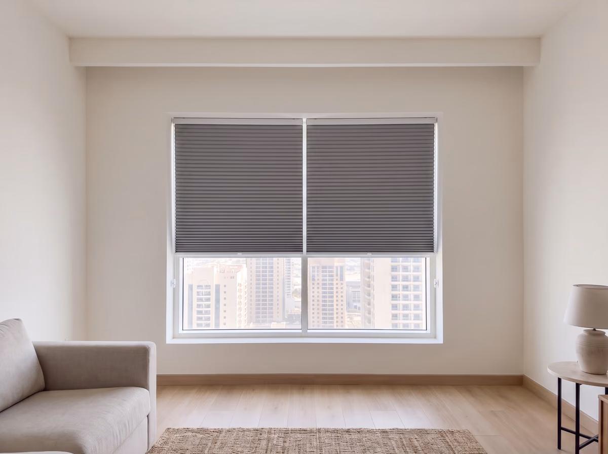 Two grey blackout honeycomb blinds lowered over half of a tower living room window inside the recess, on slim white rails