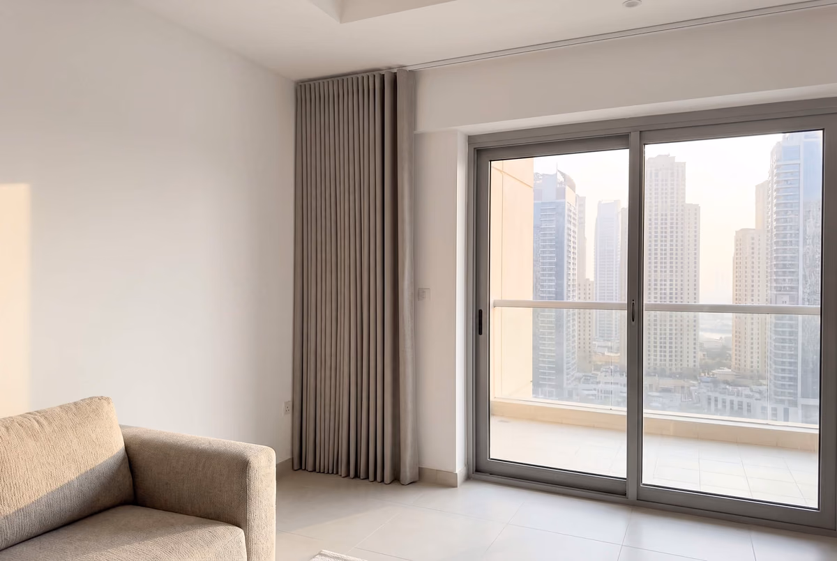 Grey wave curtain drawn fully to one side and stacked on the wall beside a sliding balcony door, high-rise towers outside