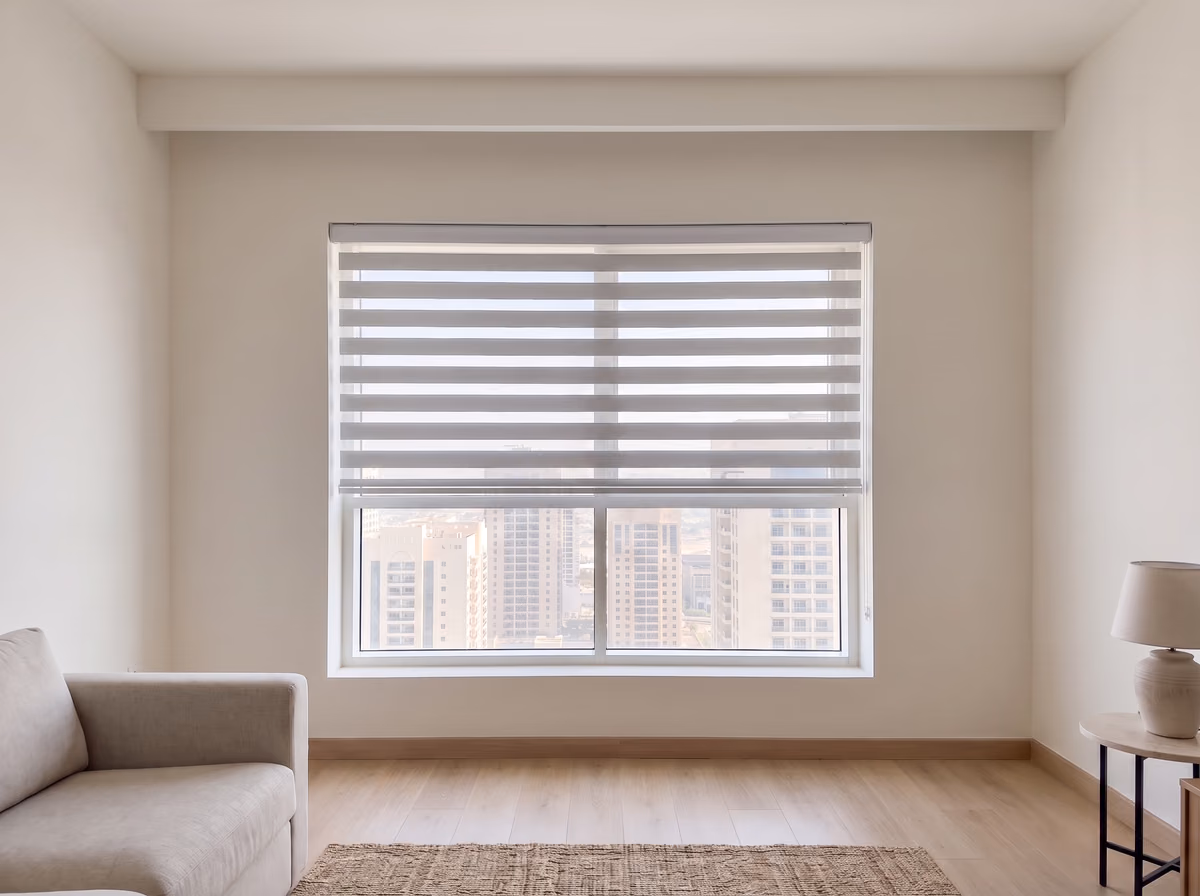 Light grey zebra blind lowered two-thirds down a living room window, its sheer stripes lined up so the towers show faintly through them