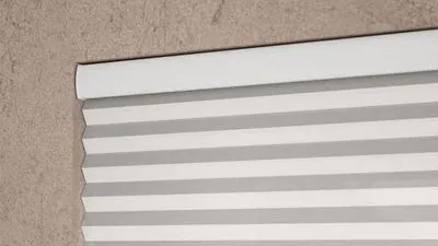 Close view of the head rail of a white honeycomb blind fixed to a wall, the cells stacked tight beneath it