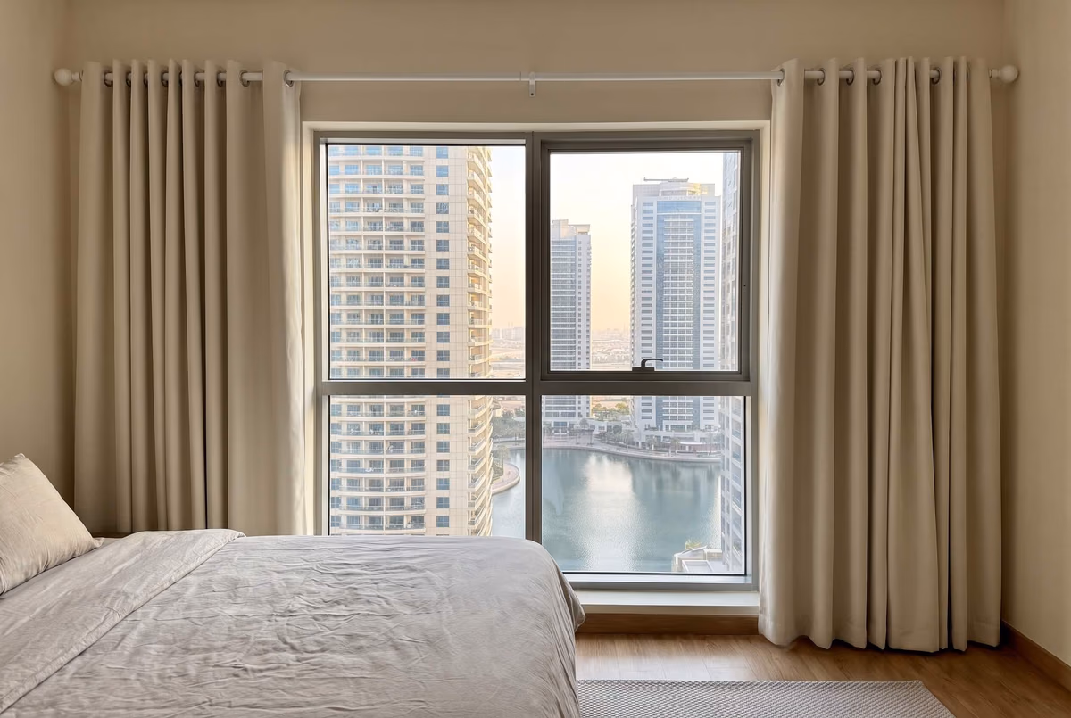 Ivory eyelet curtains on a white metal pole, drawn back from a tower bedroom window over a marina