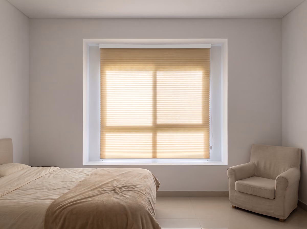 Villa bedroom with an ivory light-filtering honeycomb blind lowered inside the recess, daylight glowing evenly through its pleats