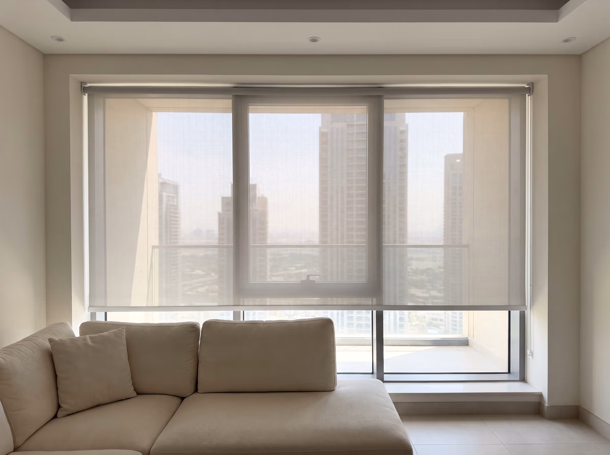 Tower living room with a light grey sunscreen roller blind lowered most of the way over wide glass, the towers showing softly through it