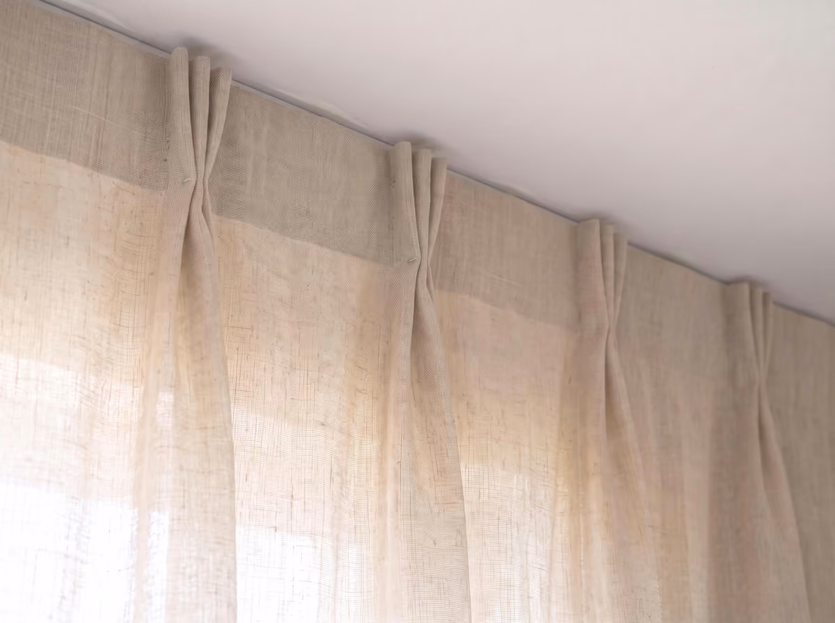 Off-white linen curtain with a pinch-pleat heading, the pleated header rising to the ceiling so the track behind it is hidden