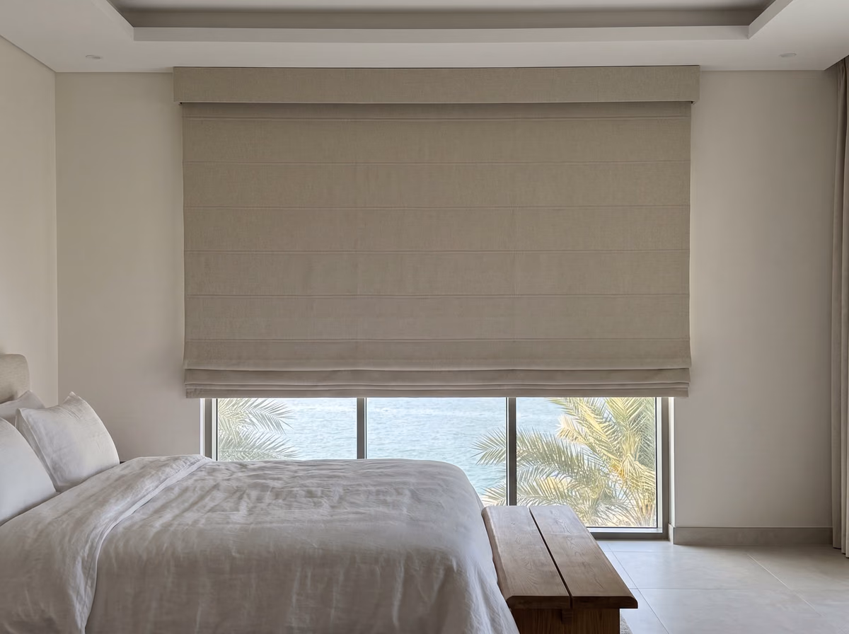 Oatmeal roman blind raised part way under a fabric pelmet, its folds gathered at the hem, the sea and palms below