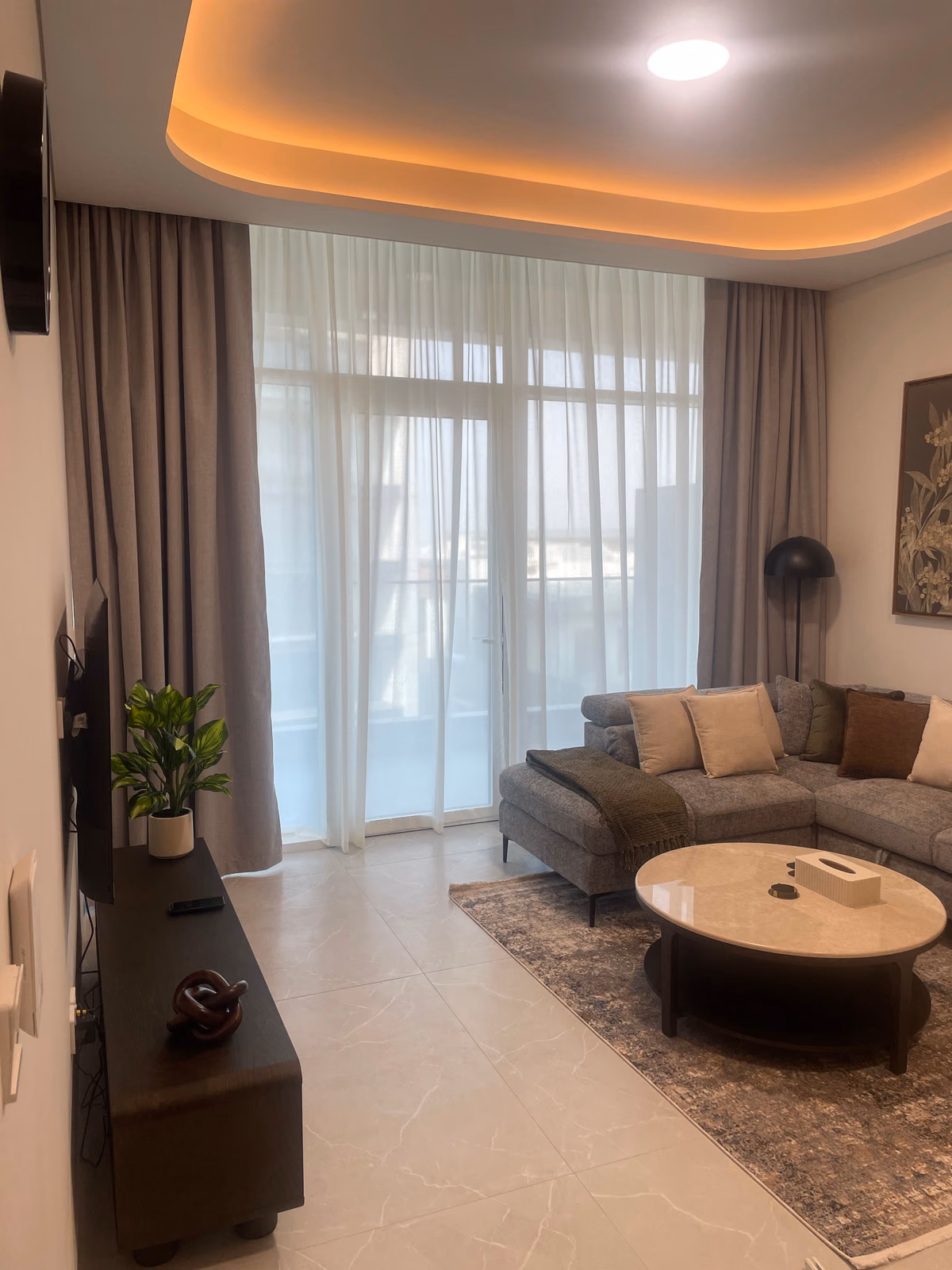 Grey pinch pleat blackout curtains and a white sheer dropping from a lit ceiling pocket to the floor of a living room, a balcony door behind the sheer
