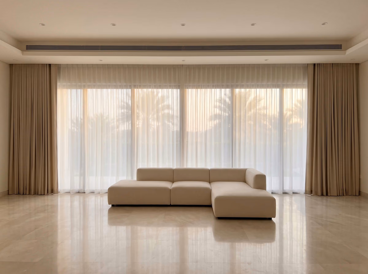 Villa living room with sheers drawn across a long wall of glass between beige ripple fold curtains, palm trees silhouetted outside
