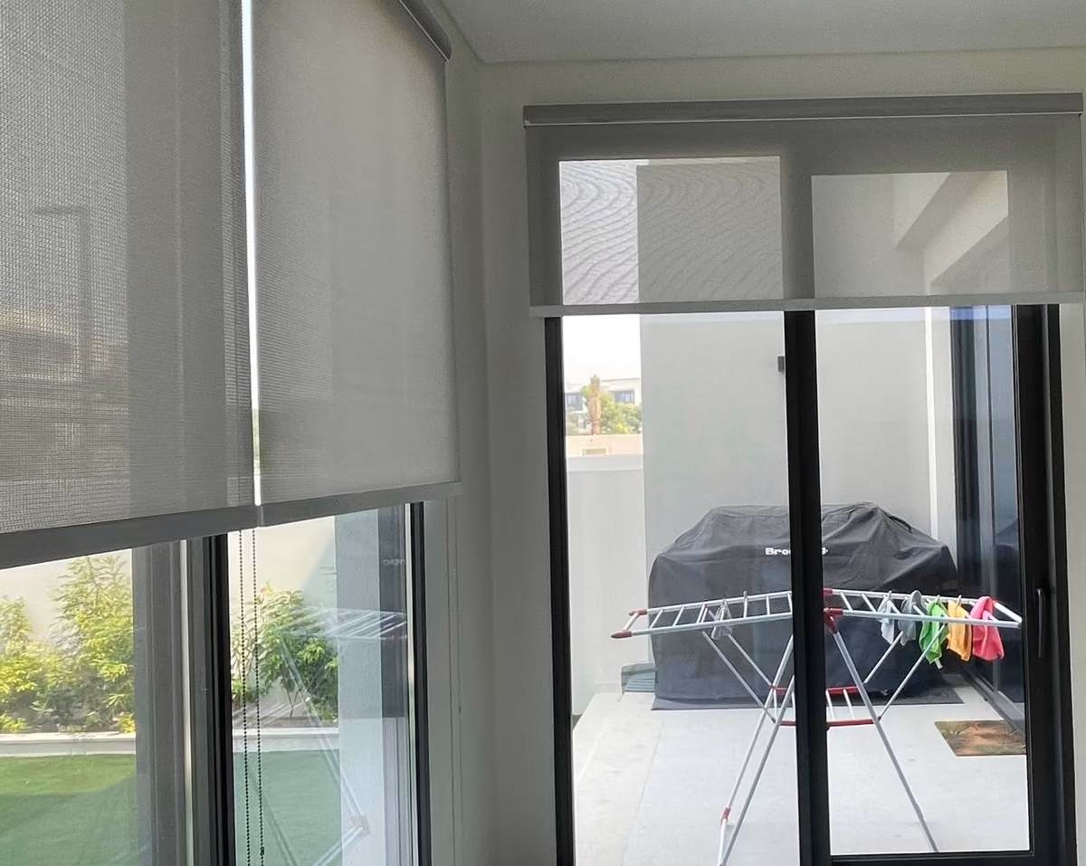 A sunscreen roller blind part lowered over a sliding door onto a covered terrace, two more sunscreen blinds over garden glass on the left