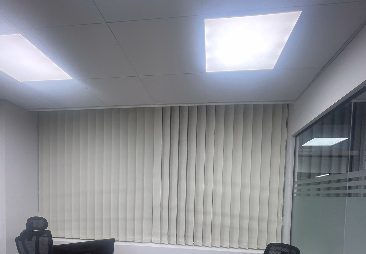 Off-white sunscreen vertical blinds drawn across the window of a two-desk office, office chairs and monitors in front