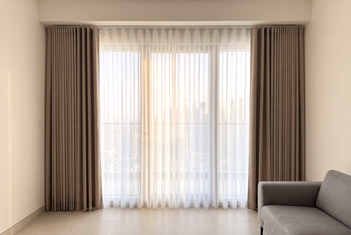 Taupe blackout wave curtains drawn to each side and a white sheer wave closed between them, both hung from a recess in a tower ceiling
