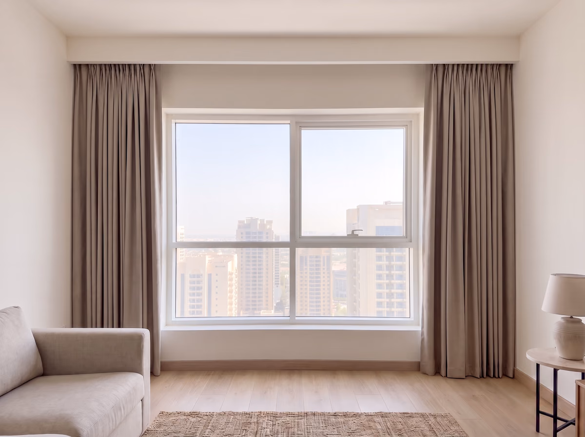 Living room window with warm taupe blackout curtains in a pinch-pleat heading drawn back to each side from a ceiling pocket, towers beyond