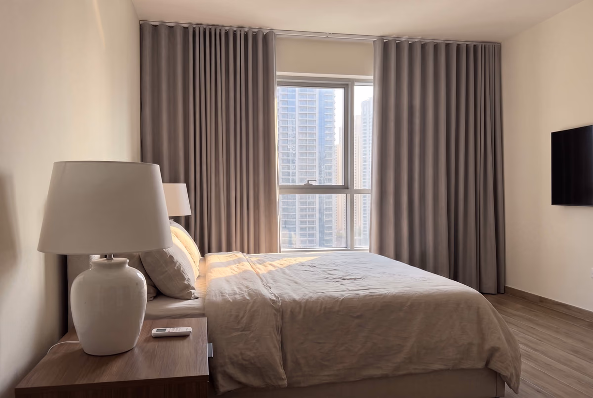 Taupe wave curtains drawn back from a tower bedroom window, morning sun across the bed