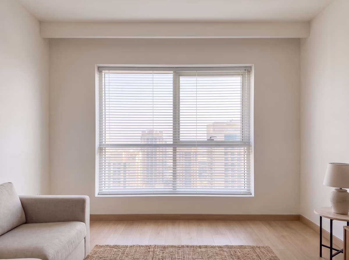 White aluminium venetian blind lowered inside a living room window recess, its narrow slats tilted half open onto the towers