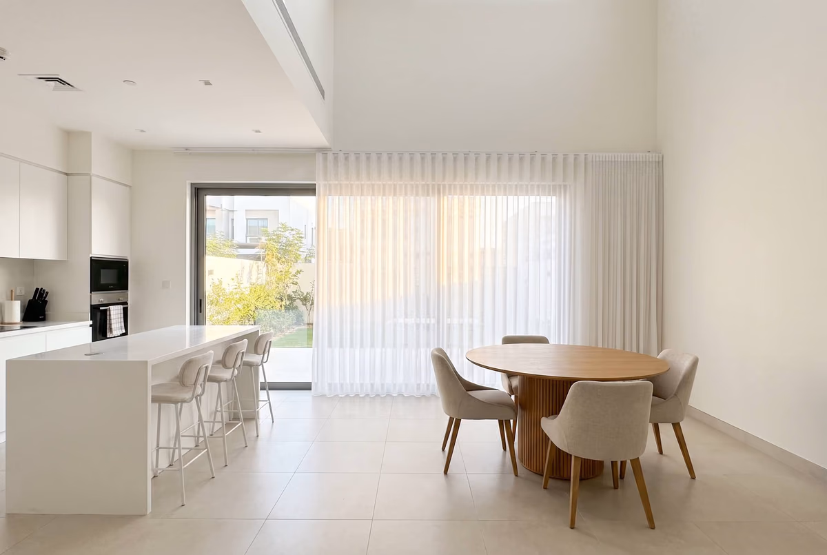 Villa kitchen-diner with a white sheer wave curtain closed across tall glass beside a garden door, a round wooden dining table in front
