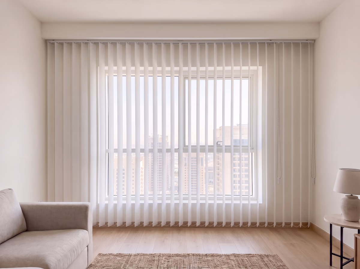 White vertical blinds hung from the ceiling across a living room window and the wall either side, the louvres turned open onto the towers