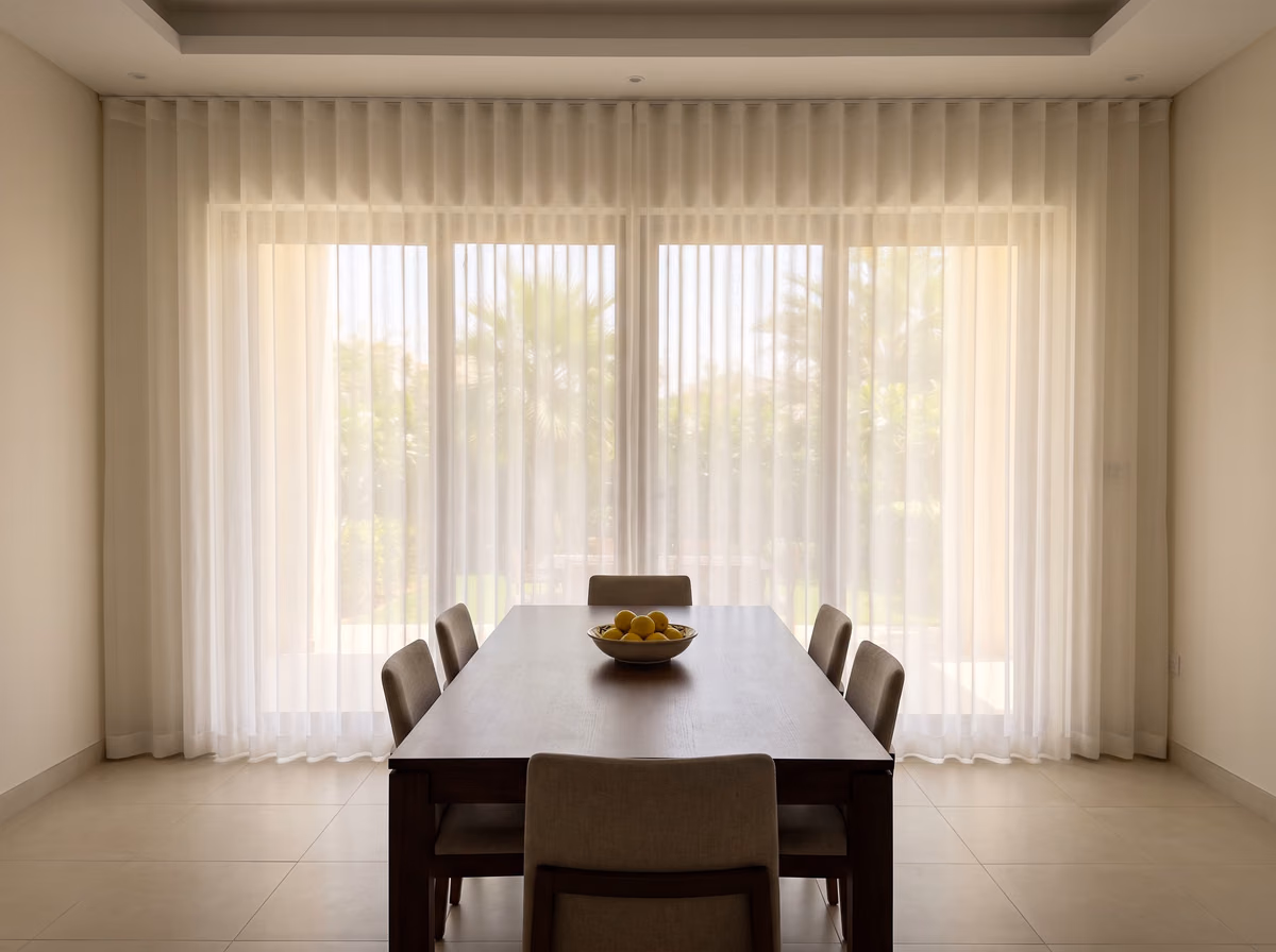 Villa dining room with a white ripple-fold sheer drawn across the glass behind a wooden table with a bowl of lemons